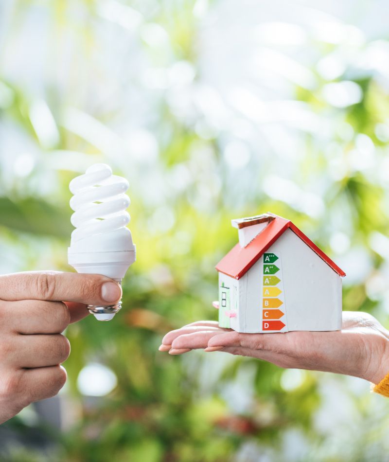 Comercialización de energía. En una mano una bombilla y en la otra una maqueta de una casa eficiente.